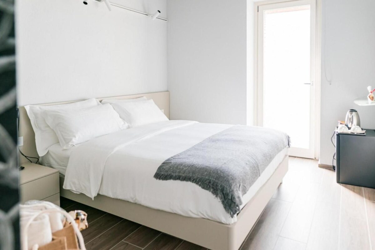 A bedroom with a bed, bedside table, and a small desk with a kettle.
