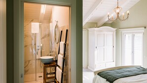 A bathroom with a large mirror, a sink, and a shower. There is a wooden chair with a towel hanging on it. The room has white walls and a wooden ceiling.