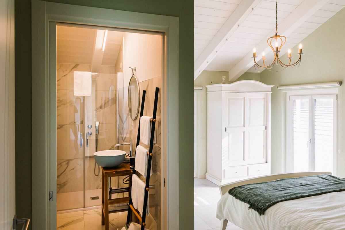 Ein Badezimmer mit großem Spiegel, Waschbecken und Dusche. Ein Holzstuhl mit einem darüberhängenden Handtuch. Die Wände sind weiß und die Decke aus Holz.