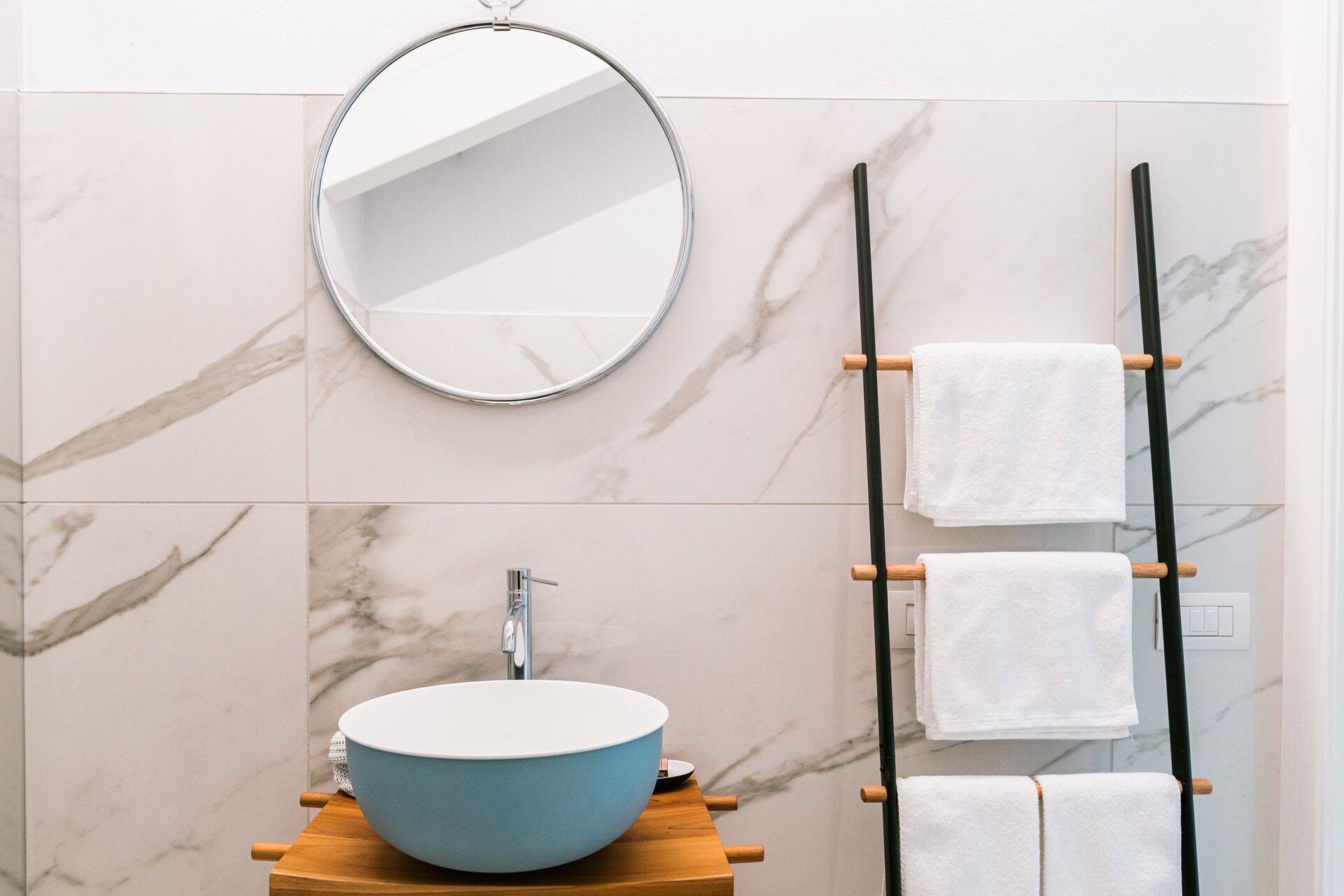 Une salle de bain avec un miroir rond, un lavabo bleu et un porte-serviettes avec trois serviettes blanches.