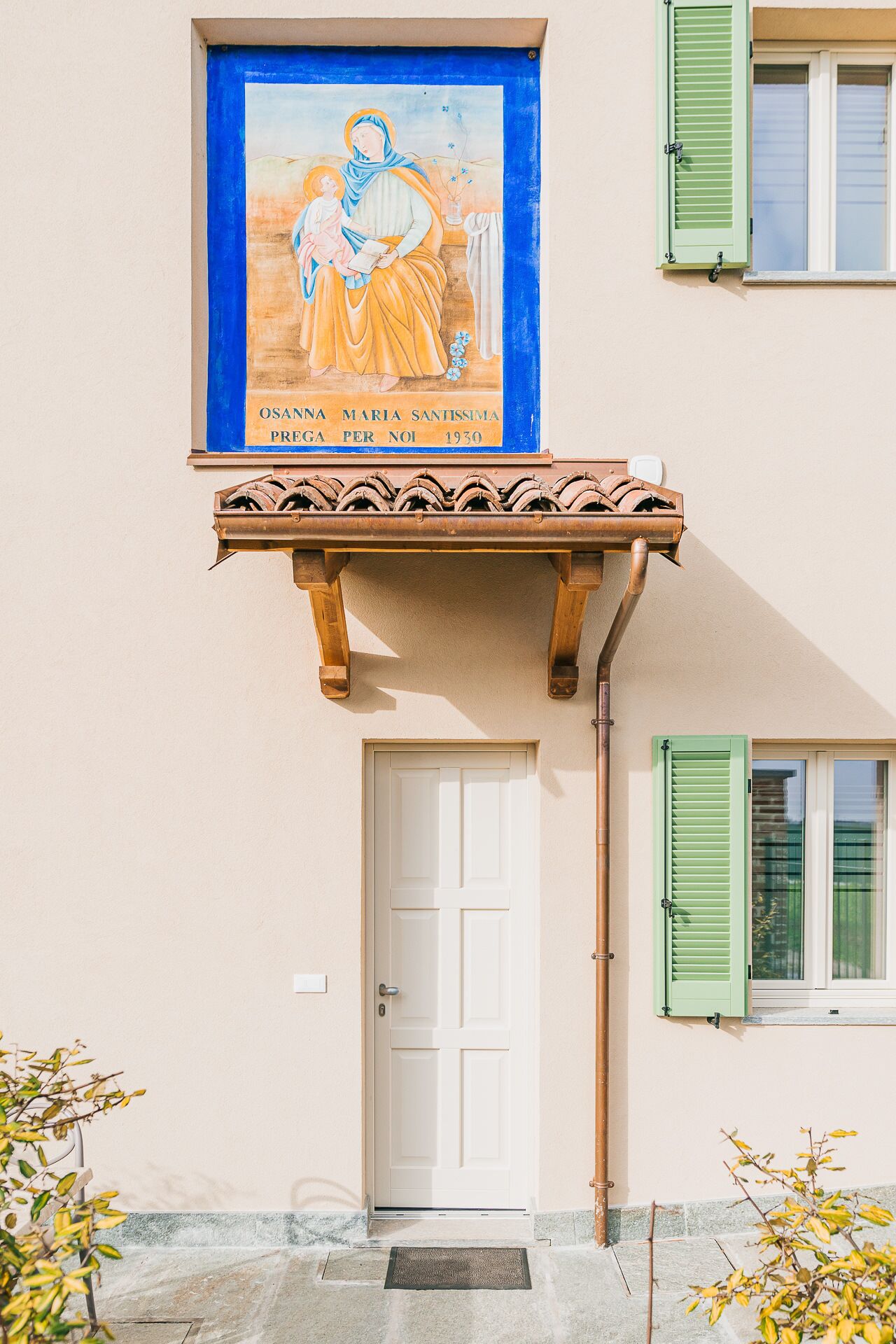 A building facade with a religious mural, a white door, and green shutters.