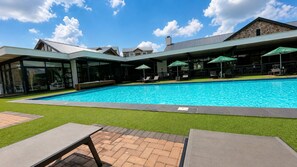 En swimmingpool med liggestole og parasoller, omgivet af en bygning med en stenfacade og et grønt tag.