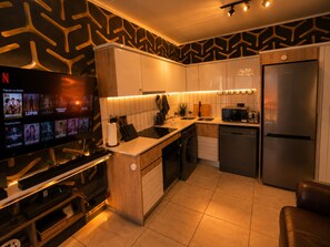 Una cocina moderna con televisor integrado mostrando contenido de Netflix, un refrigerador de acero inoxidable y una isla compacta con pileta.