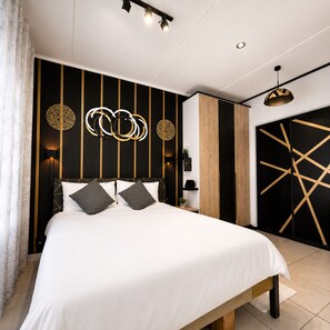 Une chambre à coucher moderne avec un grand lit, un motif géométrique sur le mur et un luminaire suspendu.