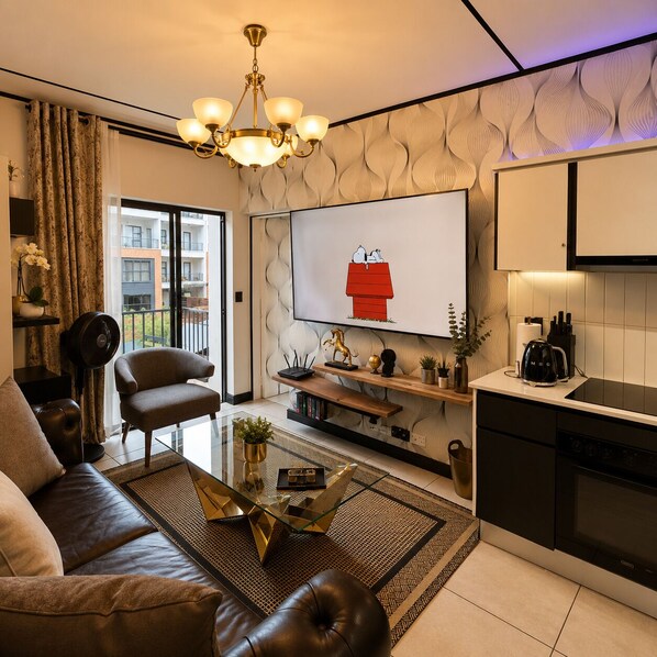 Una sala moderna con sofá, una mesa de centro, televisor y una zona de cocina con hervidor.