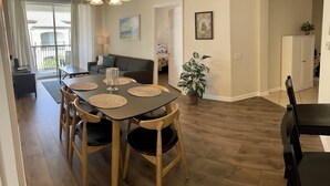 A dining area with a dark wooden table, four chairs, and a chandelier. There is a sofa and a plant in the background. - Your Home in Orlando (Orlando)
