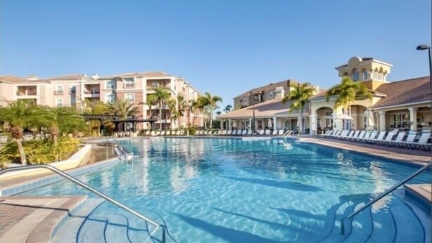 A swimming pool with lounge chairs and palm trees, surrounded by multi-story buildings. - Your Home in Orlando (Orlando)