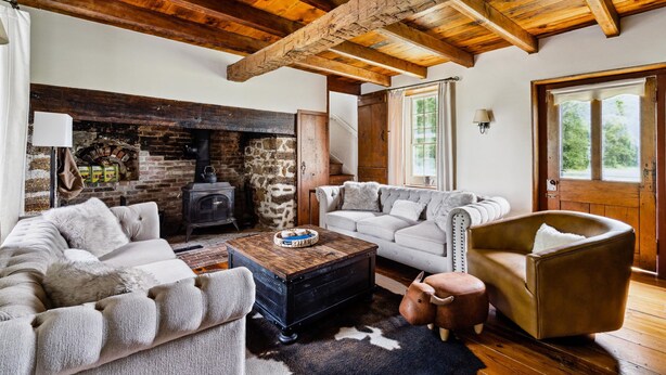 Una sala de estar acogedora con chimenea, vigas de madera, un sofá, un sillón y una mesita de centro.