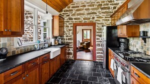 Una cocina con armarios de madera, pared de piedra y suelo de baldosas negras.
