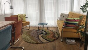 Una sala de estar con piso de madera, un sofá, una silla, una mesita y una lámpara.