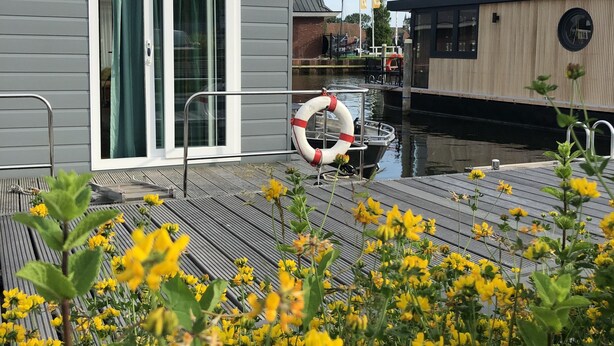 Una terraza con un flotador salvavidas, un edificio con puerta corrediza y un barco al fondo.