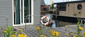 Modern houseboat in quiet harbor close to the IJsselmeer with SUPs and canoe