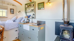 Una habitación acogedora con una cama, techo de madera, una estufa y un ventanal.