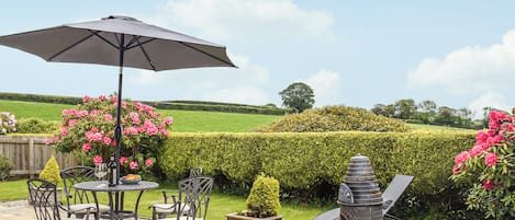 An outdoor patio with a table and chairs, a grill, and a view of the countryside.