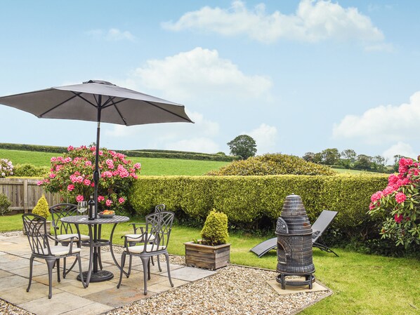 An outdoor patio with a table and chairs, a grill, and a view of the countryside.