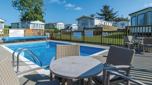 A pool area with a table and chairs, surrounded by mobile homes. - The Studio - 1 Bedroom Cabin - Amroth (Narberth)
