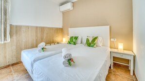A hotel room with two beds, white linens, a wooden panel wall, an air conditioning unit, and bedside lamps. - House with pool Casa Jordi in Playa de Muro (Can Picafort)
