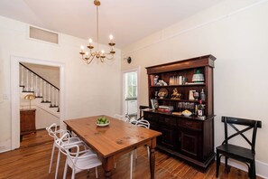A dining area with a wooden table, white chairs, a chandelier, and a dark wooden bookshelf.