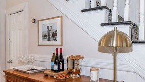 A wooden bar counter with wine bottles, glasses, and snacks. A framed picture hangs on the wall above. - Historic Charm | Near USC, Fort Jackson & 5 Points (Columbia)