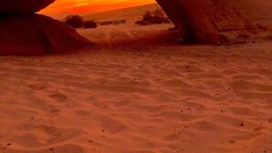 Ein natürlicher Felsbogen über einer Wüstenlandschaft bei Sonnenuntergang.