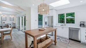 A modern kitchen with a wooden table, stainless steel appliances, and a large window overlooking greenery.