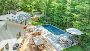 A modern house with a wooden deck, outdoor seating, and a swimming pool.