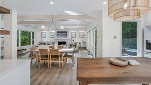 A spacious kitchen with a wooden dining table and chairs, a large window, and a hanging light fixture.