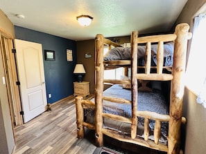 Un letto a castello con una scala in legno, un comodino con una lampada e una porta a sinistra.