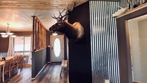 A room with a mounted deer head on the wall, wooden flooring, a dining area with chairs and a table, and a ceiling with wooden beams. - Your home away from home mountain cabin (Bayfield)