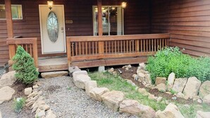 A wooden cabin with a porch, a welcome sign, and a small garden area with rocks and plants. - Your home away from home mountain cabin (Bayfield)