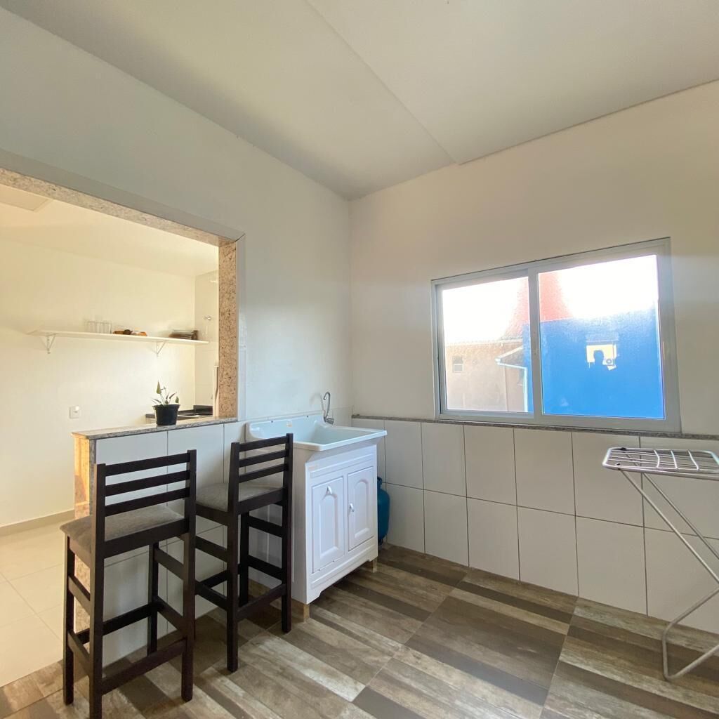 A small kitchen with a white countertop, two wooden chairs, a white cabinet, a window, and a drying rack.