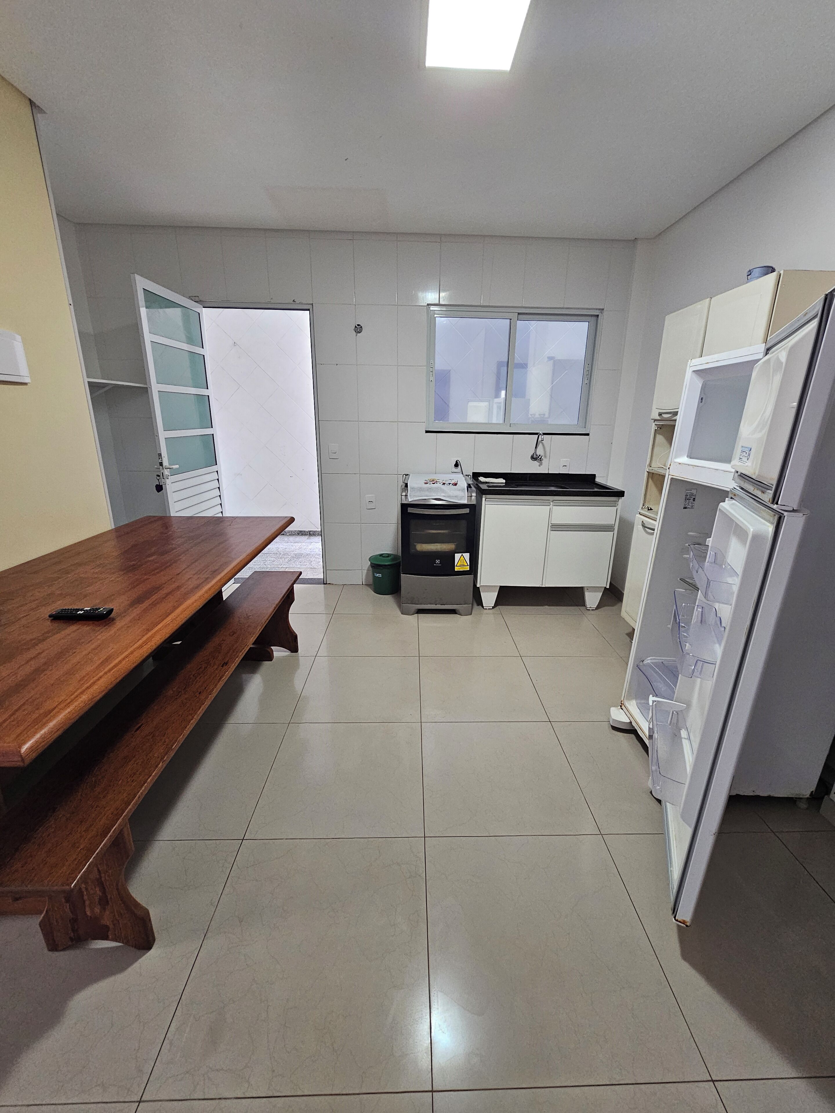 A kitchen with a wooden table, a window, a refrigerator, and a microwave.