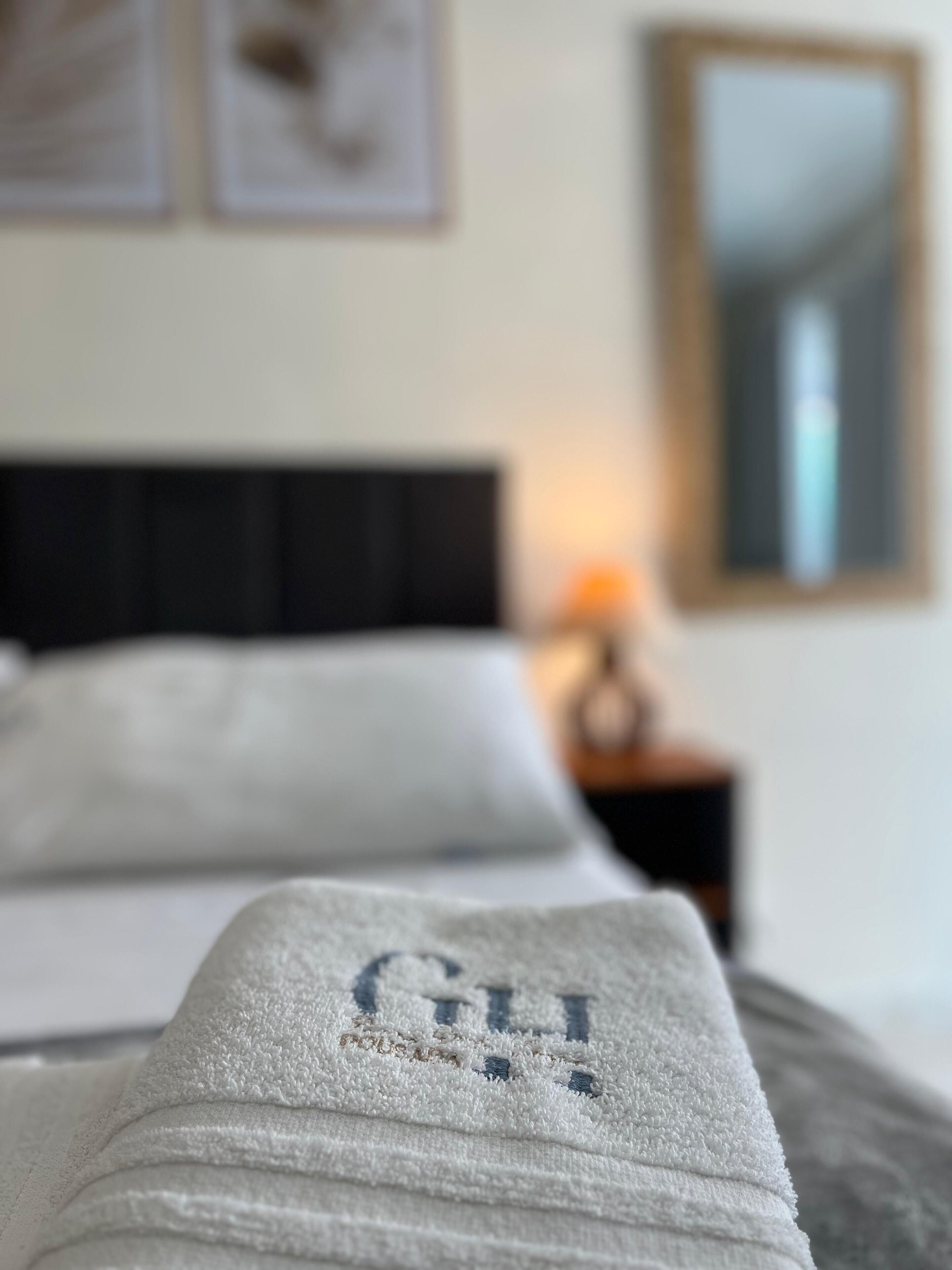 A bed with a white blanket and a pillow with embroidered text.