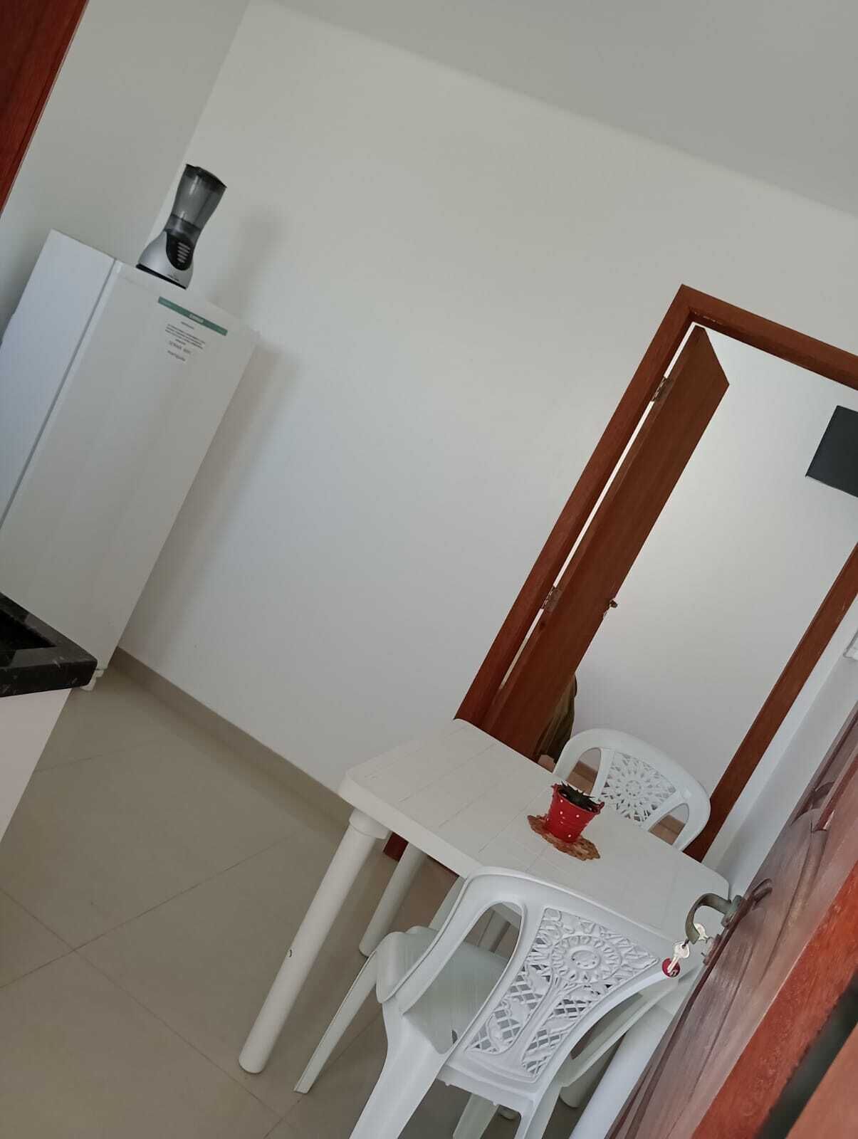 A small dining area with a white table and two white plastic chairs. There is a white cabinet with a coffee maker on top.
