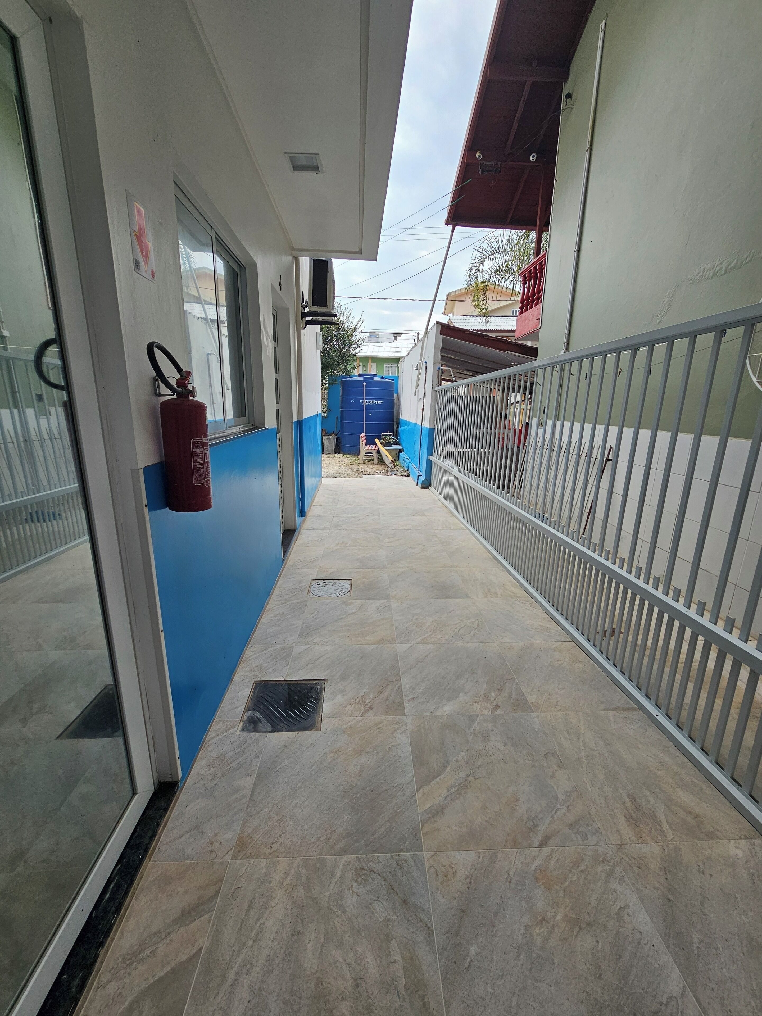 A corridor with tiled flooring, a fire extinguisher, and a blue water tank in the background.