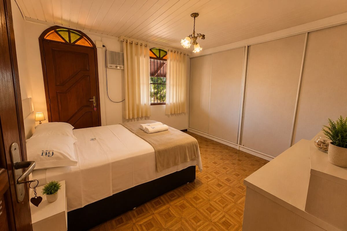 A hotel room with a bed, bedside table, lamp, window with curtains, and a ceiling light.