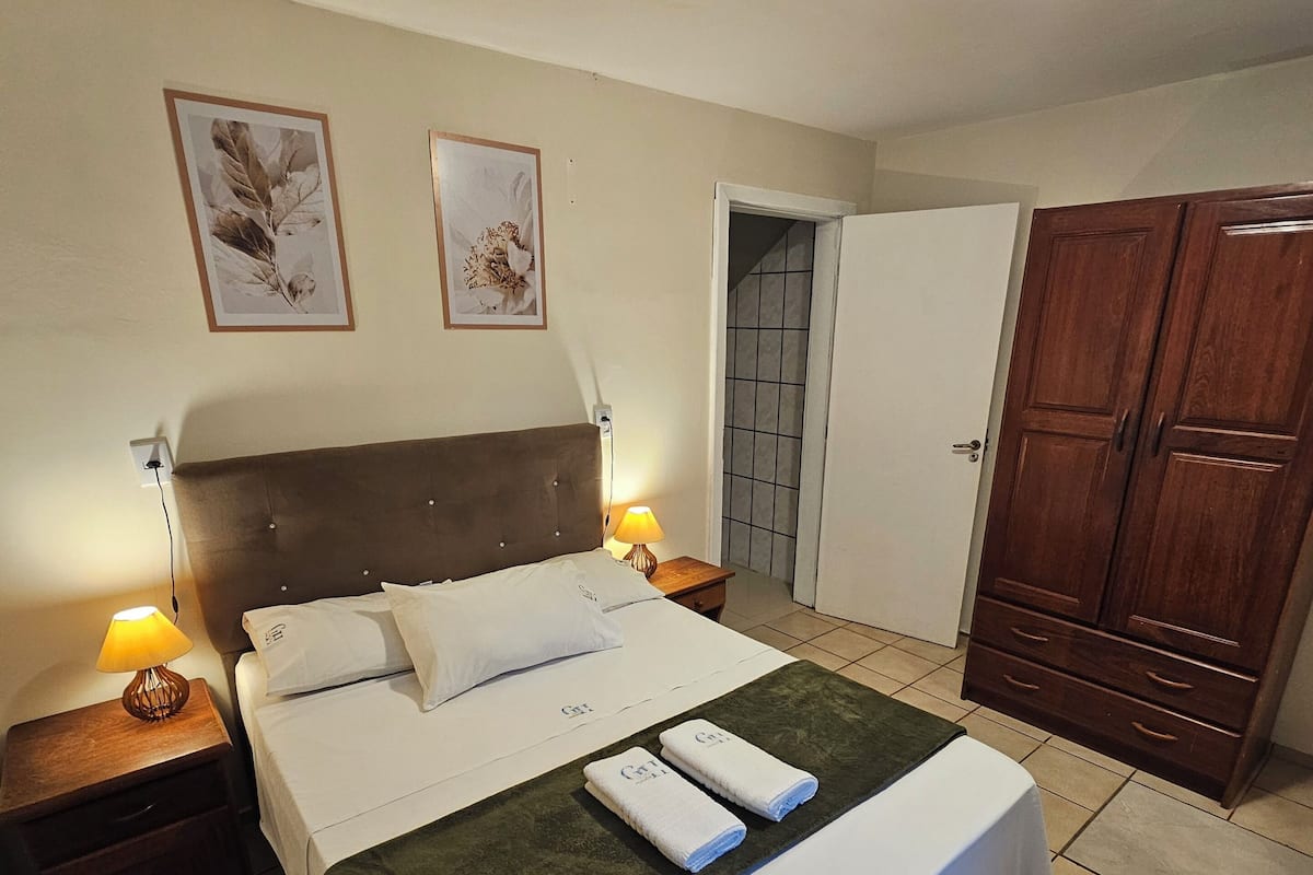 A hotel room with a bed, nightstands, a wardrobe, and a door leading to a bathroom.