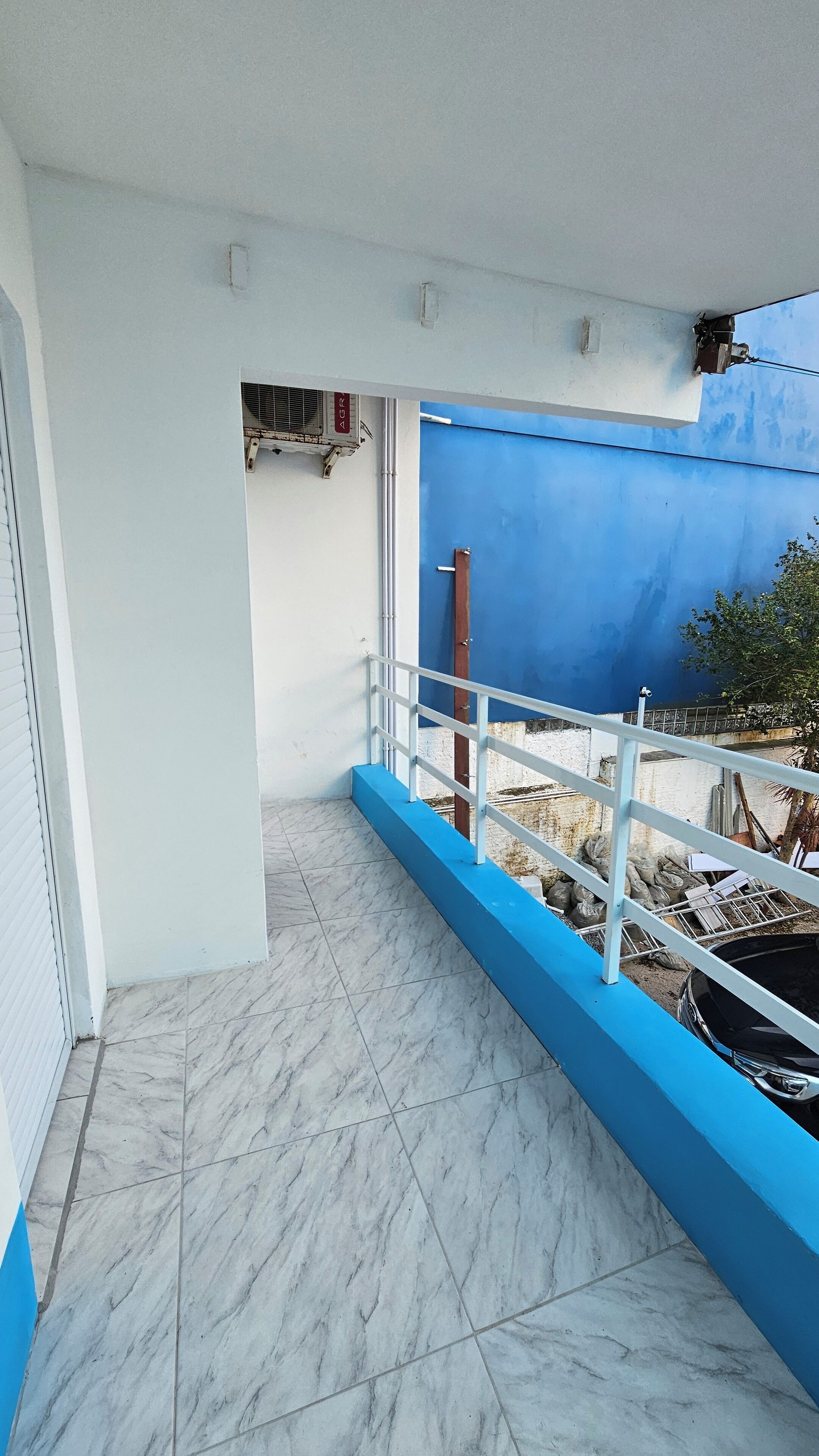 A balcony with a blue railing, white walls, and a tiled floor.