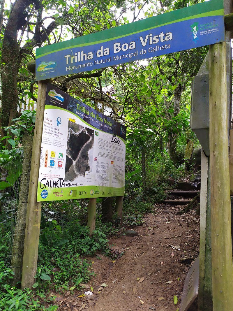A sign for Trilha da Boa Vista, a natural monument in Galheta, with a path leading through a forested area.