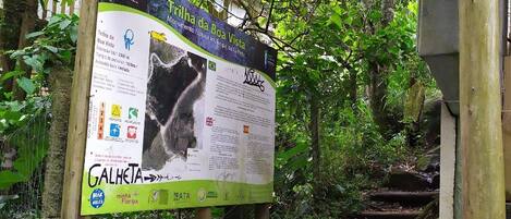 A sign for Trilha da Boa Vista, a natural monument in Galheta, with a path leading through a forested area.
