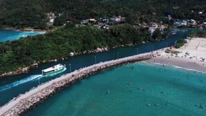 An aerial view of a coastal area with a pier, a boat, and a beach. - GH Barra da Lagoa (Florianópolis)