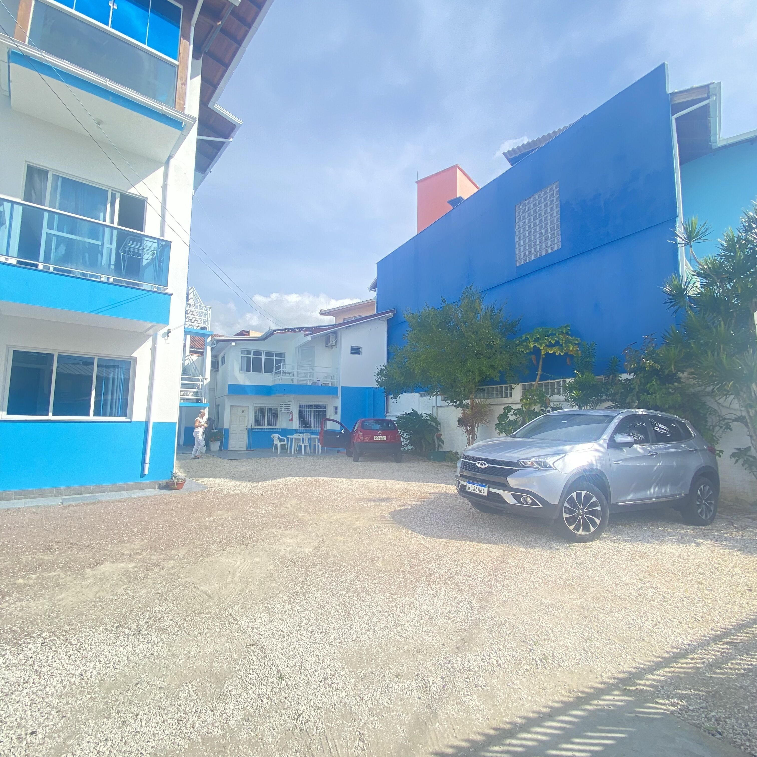Un barrio residencial con un edificio azul, un coche rojo y un SUV plateado estacionados en un camino de grava.