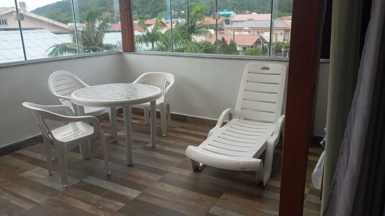 A balcony with a round table and four chairs, a single lounge chair, and a view of buildings and palm trees through large windows.