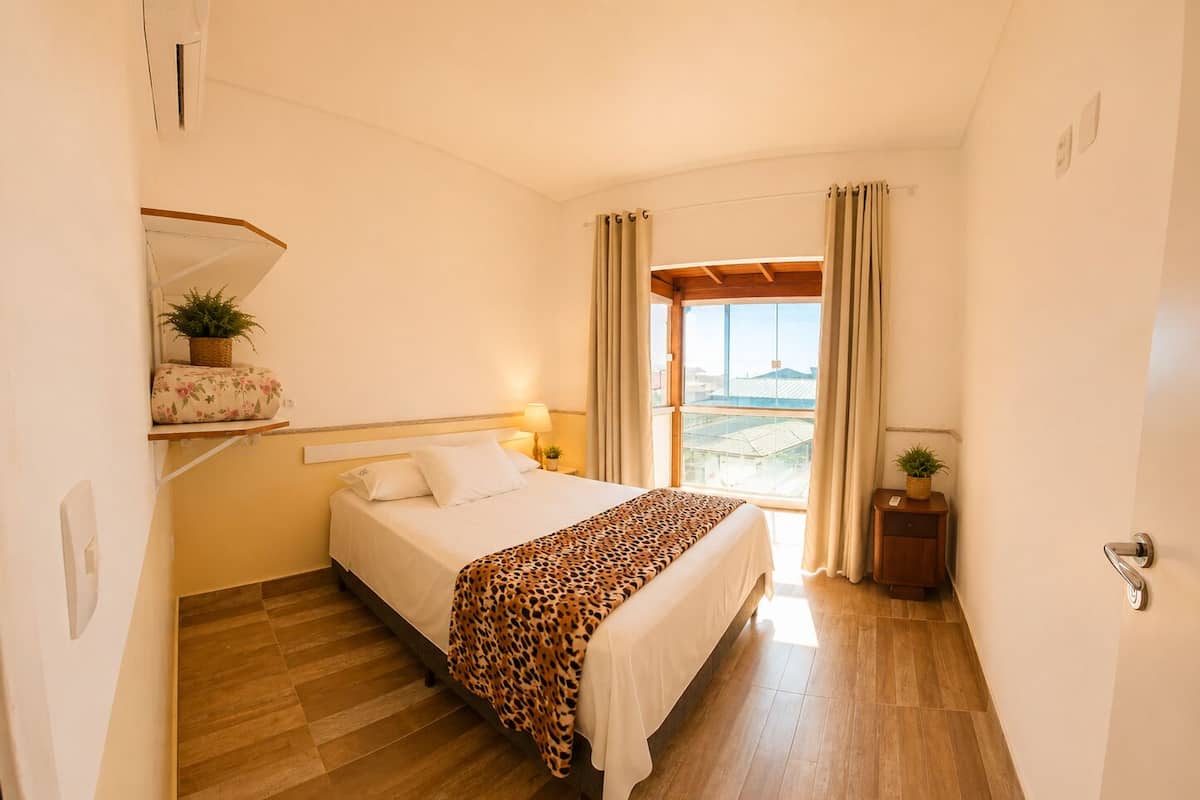 A hotel room with a bed, a nightstand, a window with curtains, and a view of the outside.