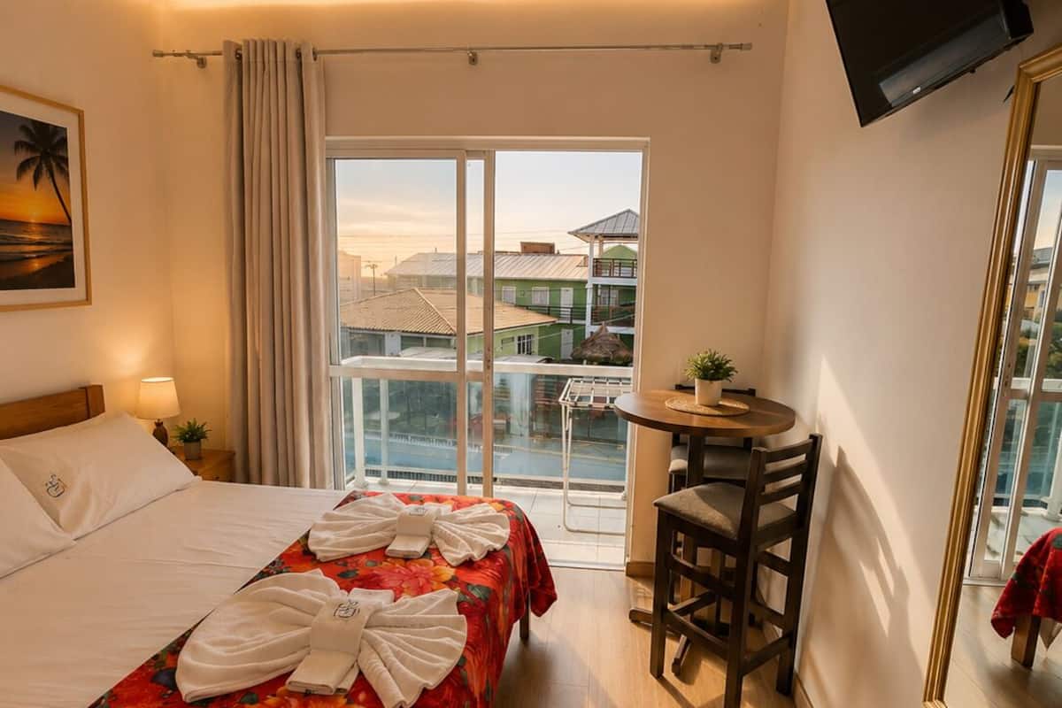 A hotel room with a bed, a desk, a TV, and a balcony with a view of buildings.