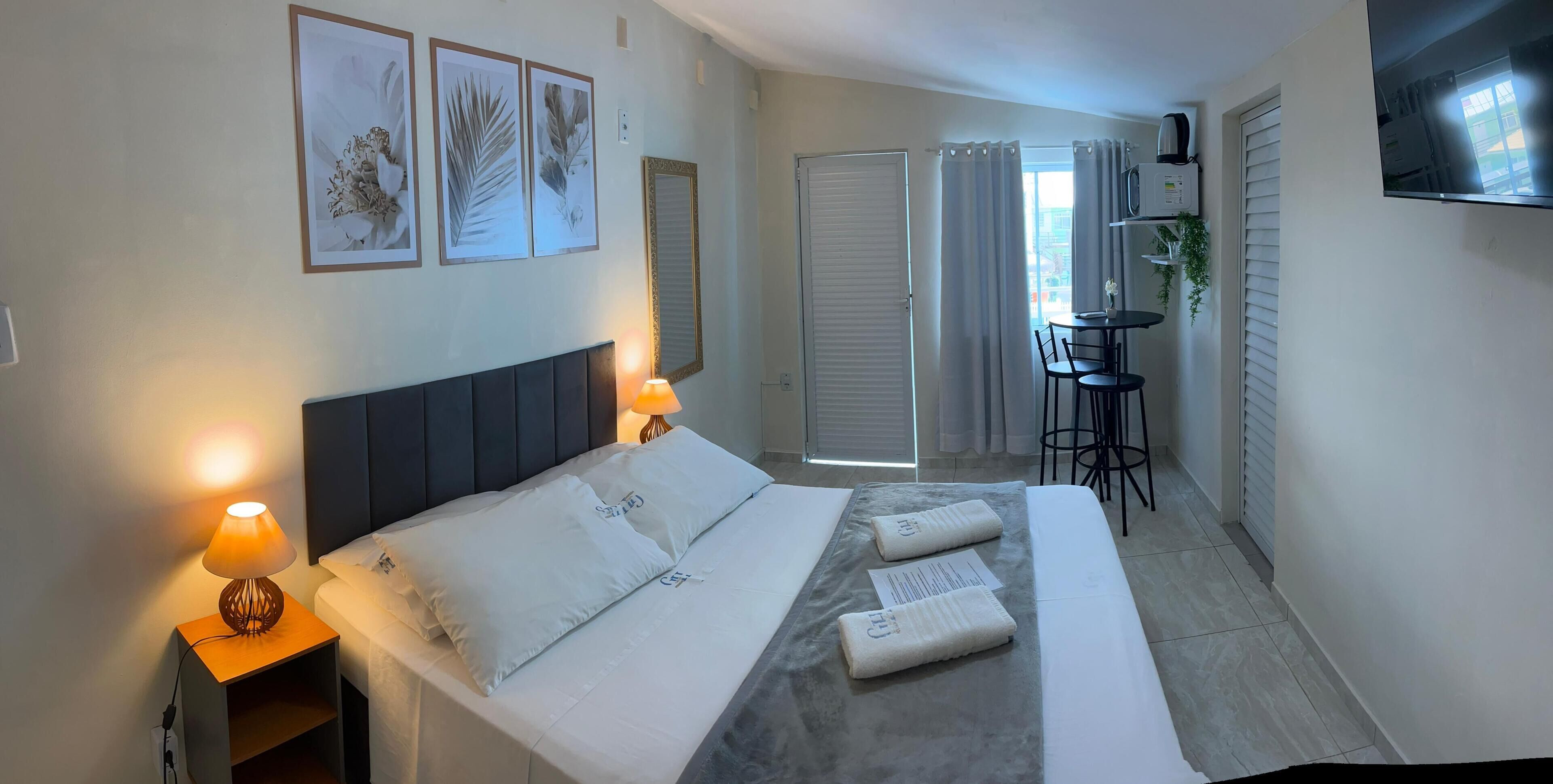 Une chambre d’hôtel équipée d’un lit, de lampes de chevet, d’une petite table, d’une chaise et d’un téléviseur fixé au mur.