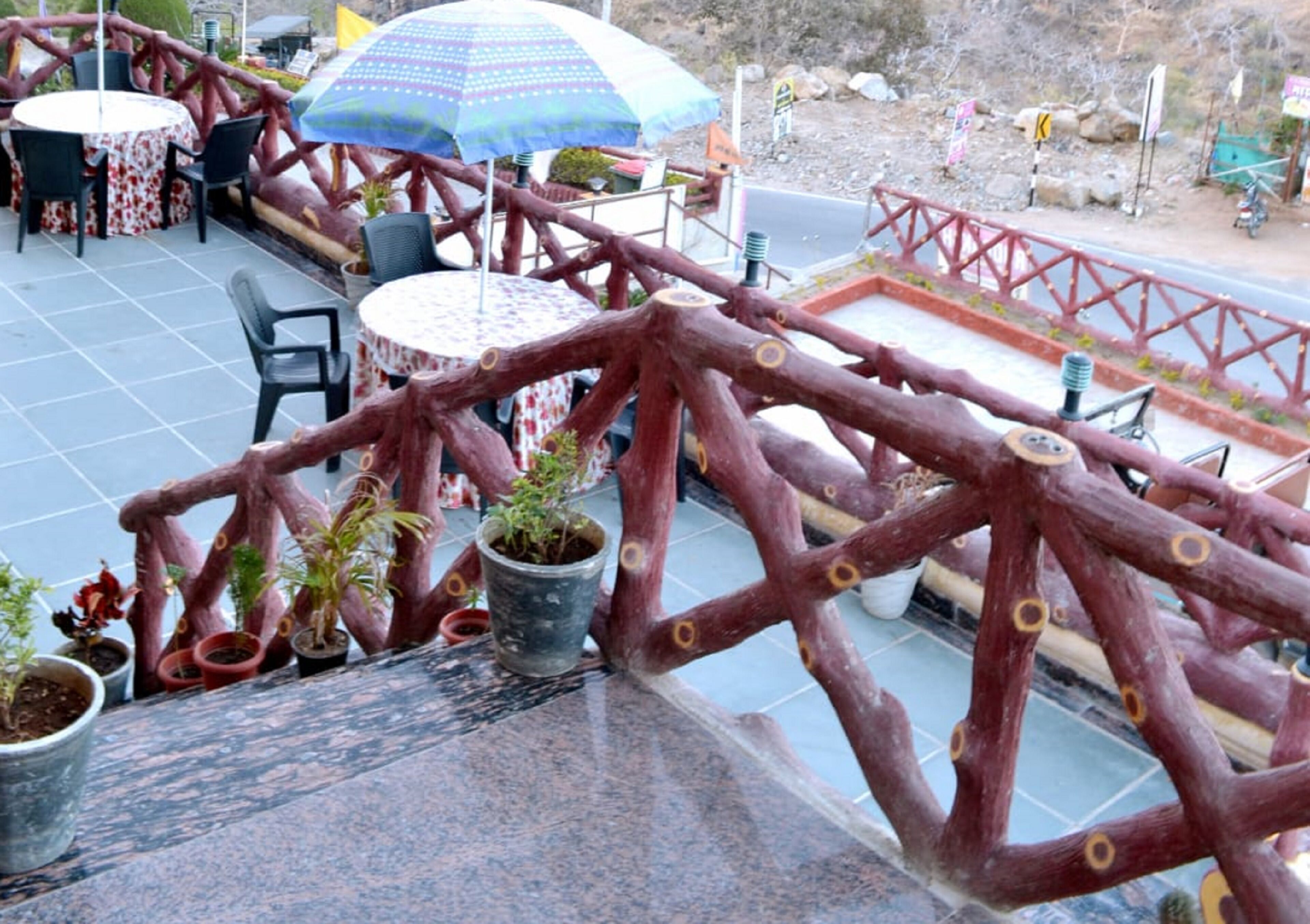 Un patio al aire libre con mesas y sillas, plantas en macetas y una barandilla de madera roja.