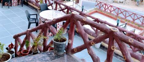 Un patio al aire libre con mesas y sillas, plantas en macetas y una barandilla de madera roja.