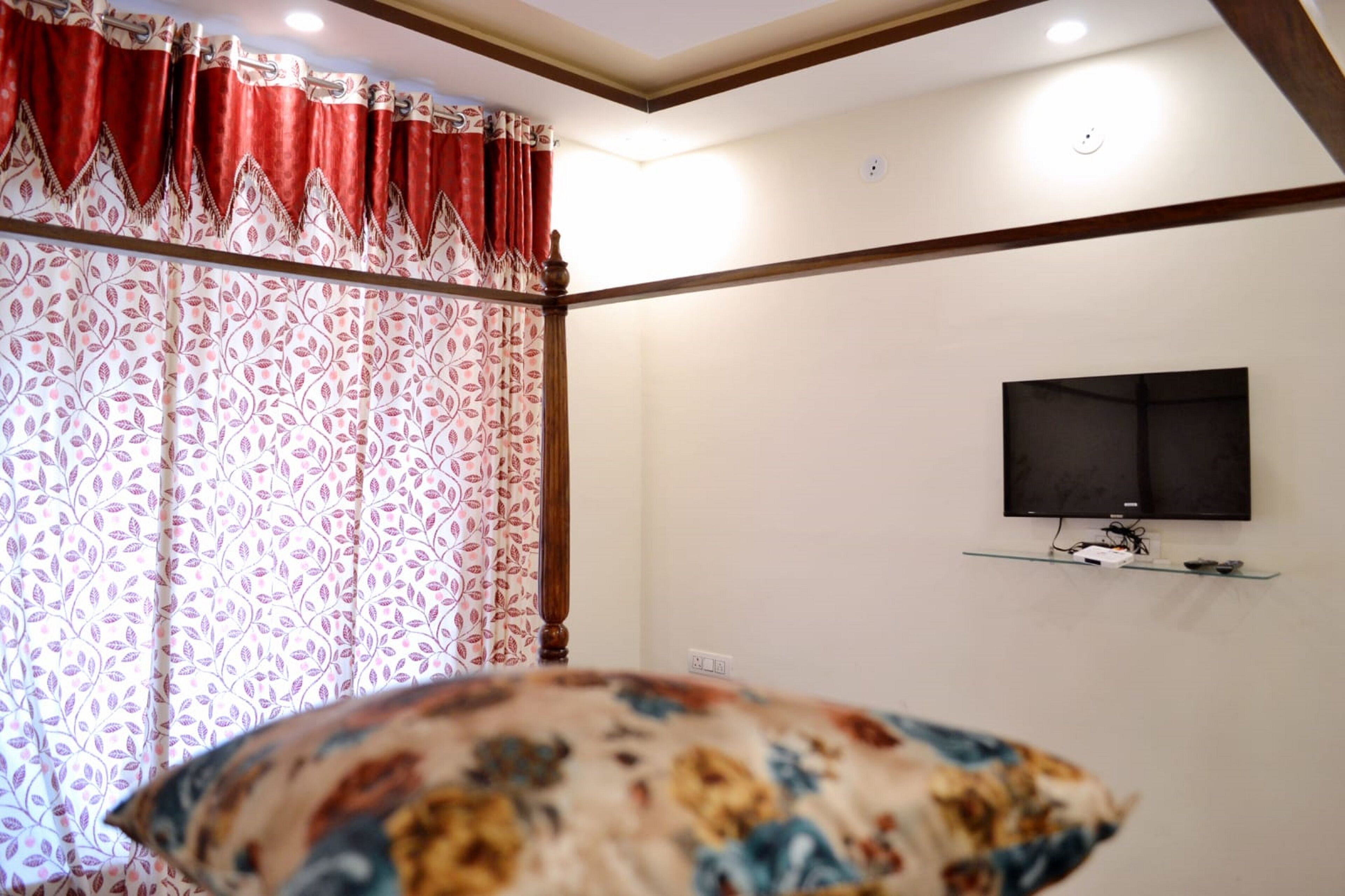 A room with a bed, a TV mounted on the wall, and a window with patterned curtains.