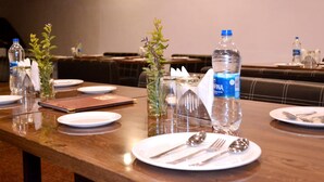 Une table à manger dressée avec des assiettes, des couverts et des bouteilles d’eau, agrémentée d’un vase de verdure et d’un bocal en verre placé au centre.